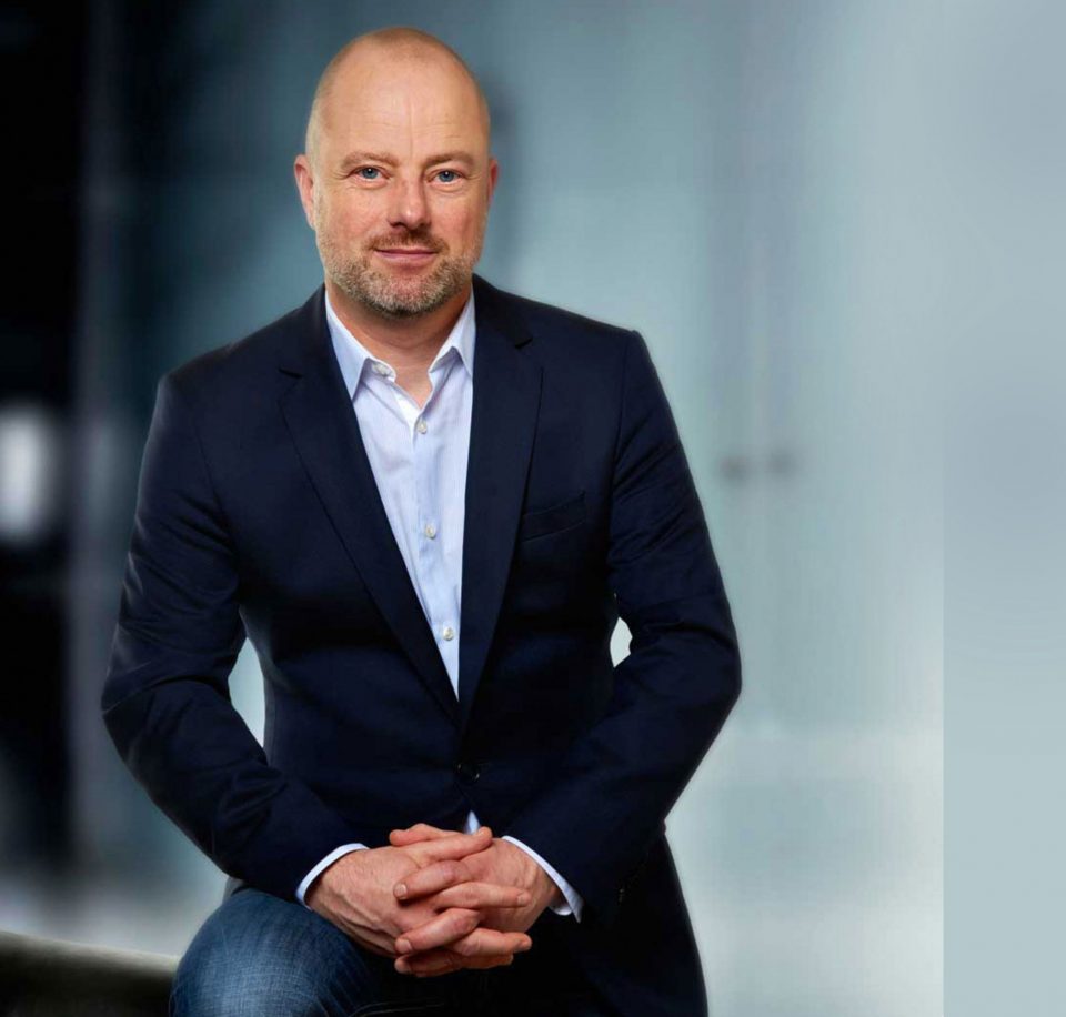 Jochen von der Lieth, sitzend im dunkelblauen Sakko vor einer hellen Glasfassade